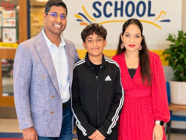 A family smiling together in front of a school sign indoors.