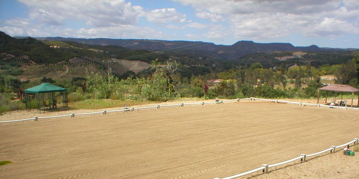 Open field with fenced sandy ground and gazebos in a mountainous area.