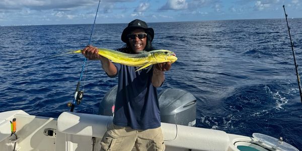Man on boat proudly holds a bright yellow fish he caught at sea.
