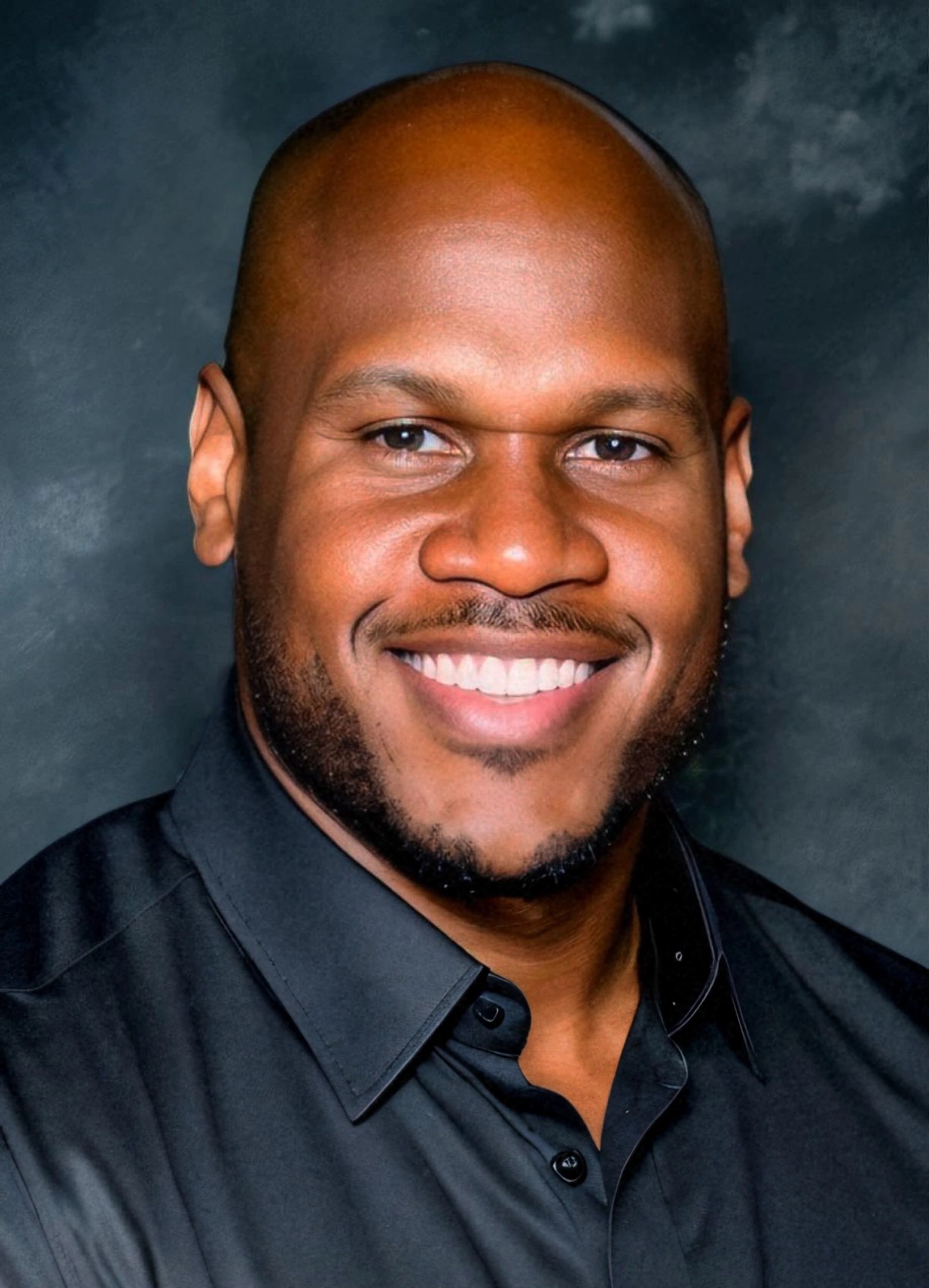 Smiling bald man with a trimmed beard wearing a black shirt.