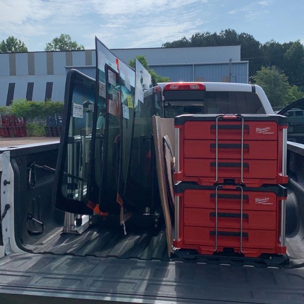 Pickup truck bed loaded with glass panels and red Milwaukee toolboxes.