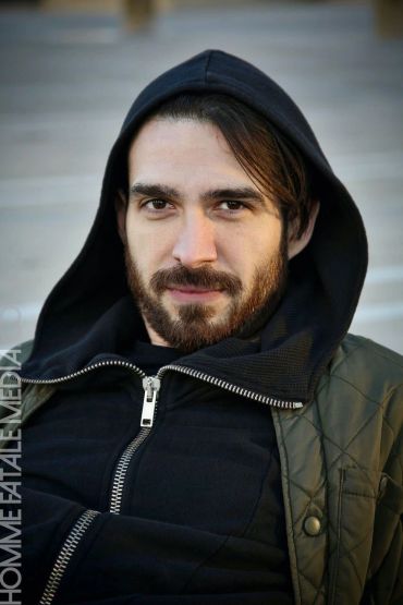 Man with beard wearing a black hoodie and jacket.