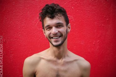 Smiling shirtless man against a red wall.