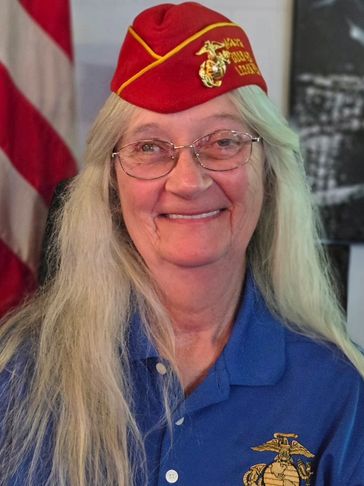 Smiling woman in a Marine Corps League hat and blue shirt with emblem.