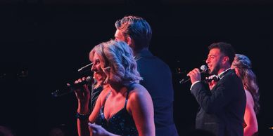 Four singers performing on stage with microphones under dramatic lighting.