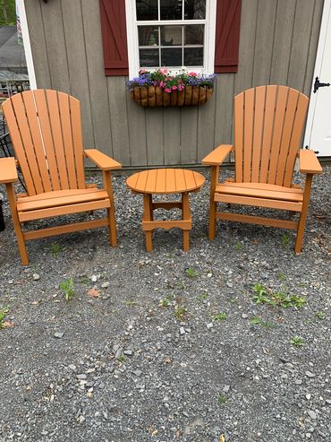 Two wooden chairs and a small table outside against a house wall.