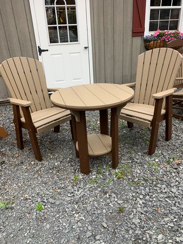 Two beige Adirondack chairs with a round table outside a building.