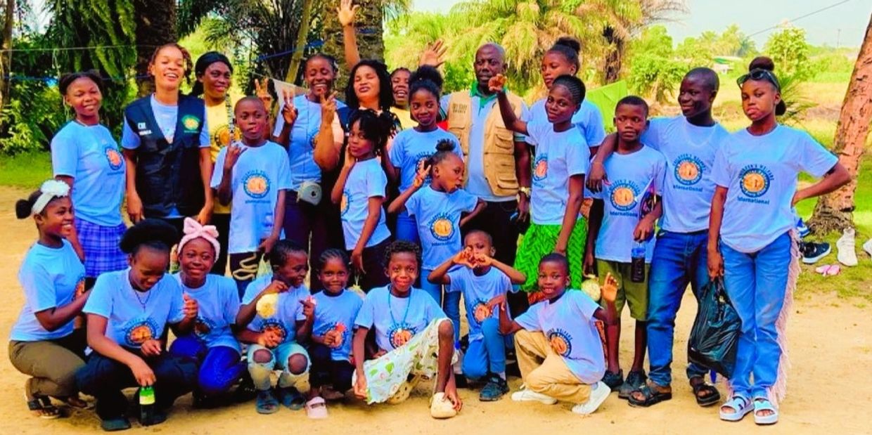 A large group of children and adults posing outdoors, many wearing matching blue shirts.