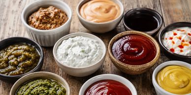assortment of sauces and dips in small bowls on a rustic board
