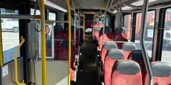 Interior of an empty bus with red seats and yellow poles.