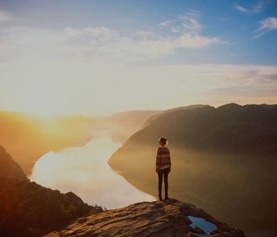 Person standing on a cliff overlooking a river at sunrise.