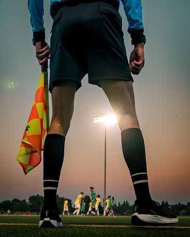 A soccer referee holding a flag during a game at sunset.