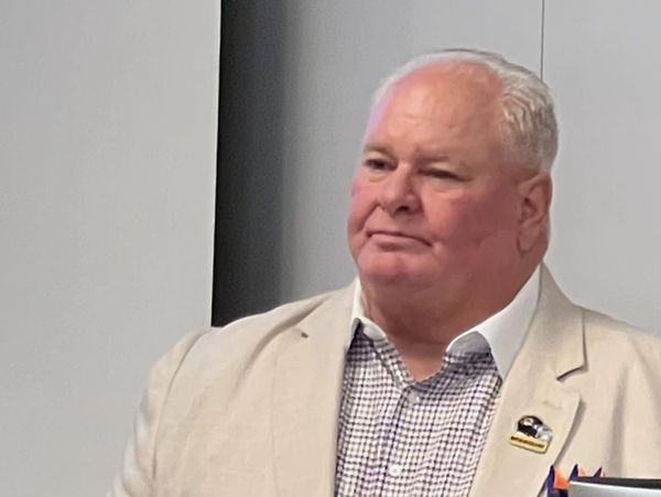 Elderly man in a beige blazer and checkered shirt.