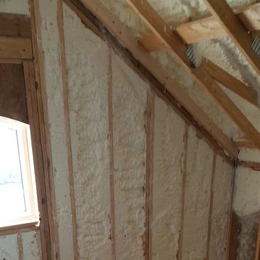 Spray foam insulation applied between wooden wall studs in an attic.