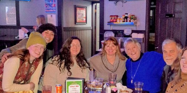 A group of six people smiling around a restaurant table with drinks and food.