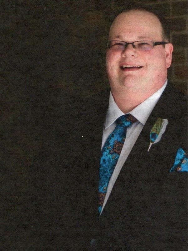 Man in suit with blue patterned tie and boutonniere smiling.