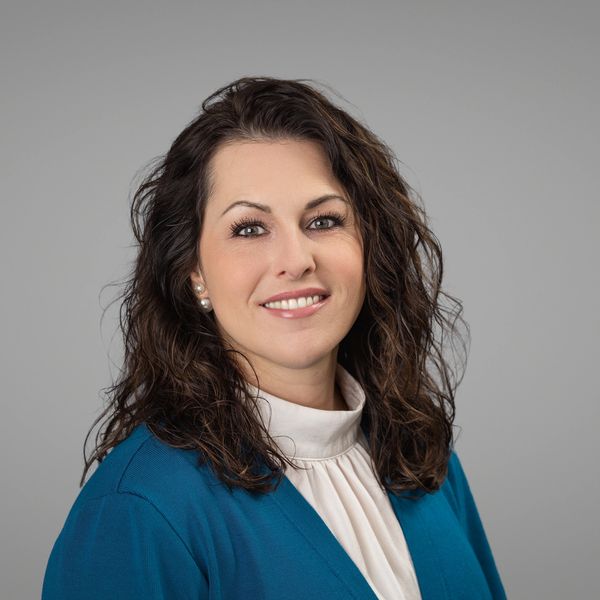Smiling woman with curly hair in blue blazer and white blouse.
