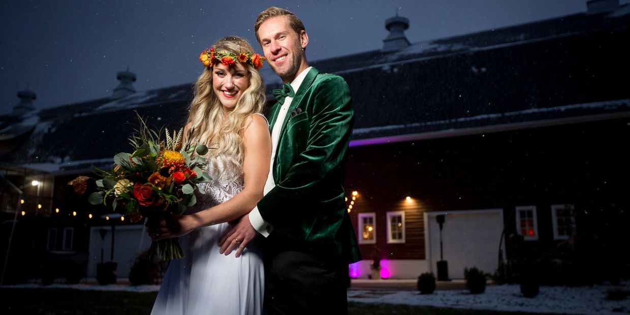 A bride and groom smiling outdoors at night in winter, with the bride holding a colorful bouquet.