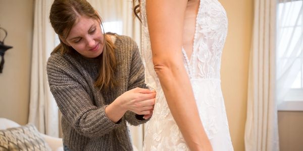 Wedding dress appointment helping bride with zipper.