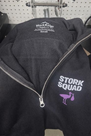 Black zip-up jacket with "STORK SQUAD" logo and stork graphic.
