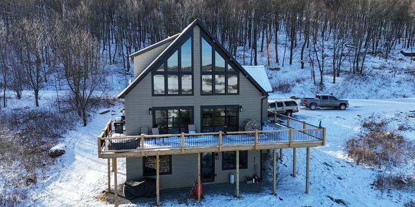 Snow-covered modern cabin with large windows in a wooded winter landscape.