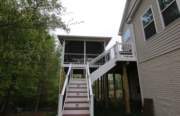 Raised wooden deck with stairs and screened porch attached to a house.