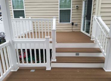 A clean, brown wooden deck with white railings and steps leading to a house.