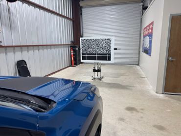 Blue car in a garage with a calibration board.