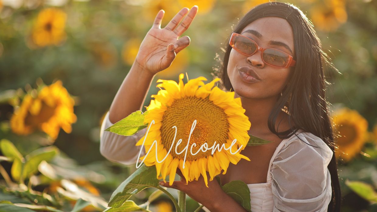 Photo of beautiful black woman in sunflower field welcoming visitors