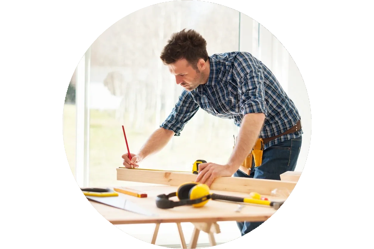 Man bent over a workbench measuring a piece of wood and marking with a pencil.