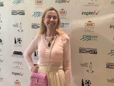 Woman posing at a Cine@Art event with logos on backdrop.