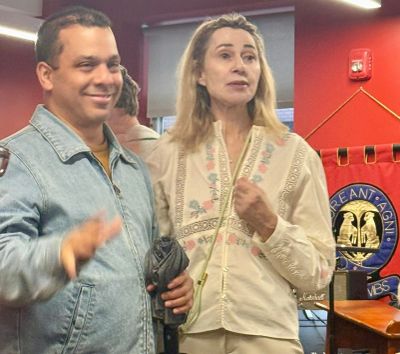Two people posing indoors, one waving.