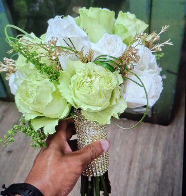 Hand holding a bouquet of white and pale green flowers.