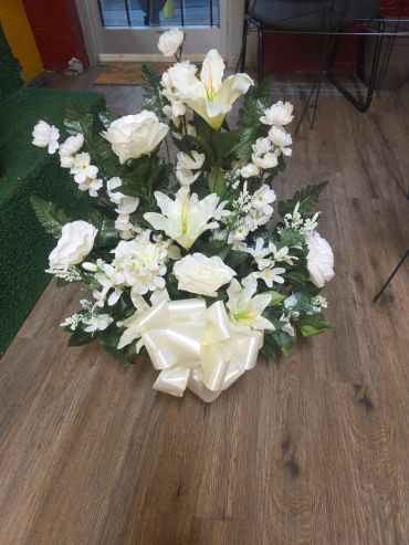 White floral arrangement with lilies and roses on a wooden floor.