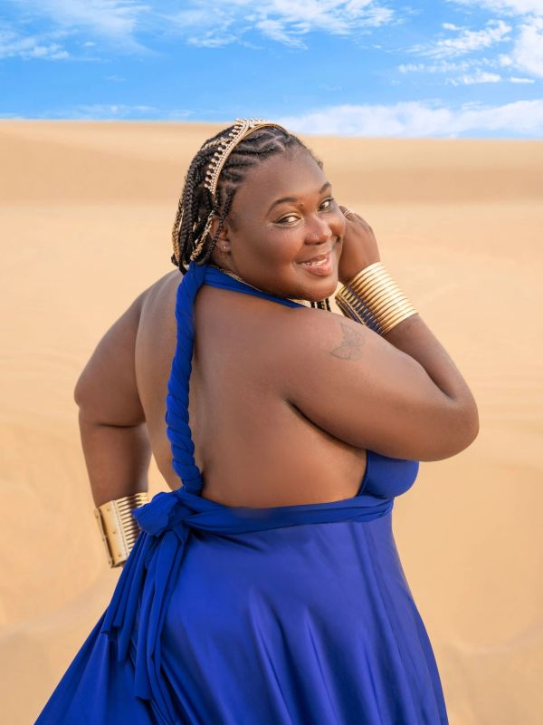 Smiling woman in blue dress standing in desert.