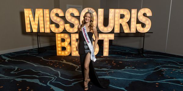 Miss Missouri Best winner posing in front of illuminated sign.