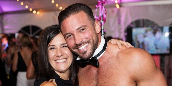 Smiling woman posing with a shirtless, bow-tied man at a festive event.