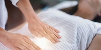 Person receiving healing or energy therapy with hands glowing over abdomen.