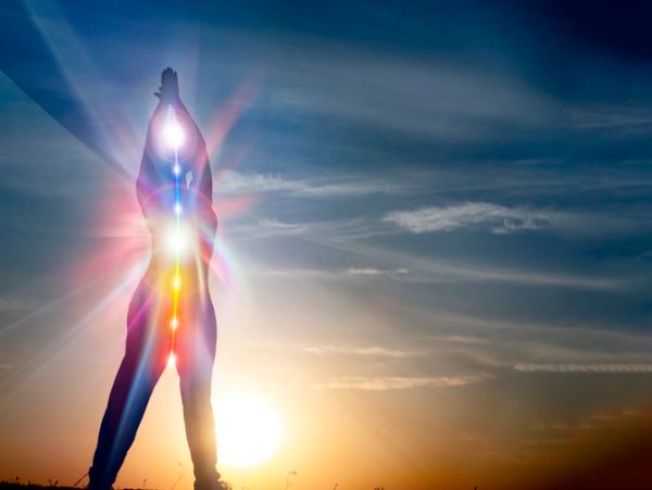 Silhouette of a person with glowing chakras against a sunset sky.