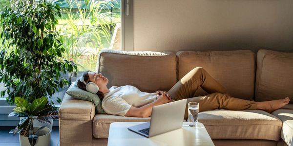 A woman resting on a couch with headphones, representing an online Nervous System Reset session.