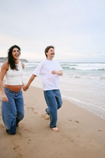 Couple laughing and holding hands while walking barefoot on the beach.