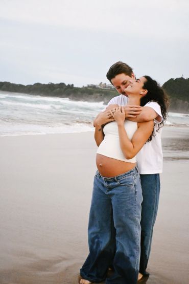 Pregnant woman and partner embracing on a beach, sharing a joyful moment.