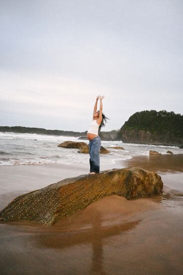 A woman stretching on a rock at the beach with waves and cliffs in the background.