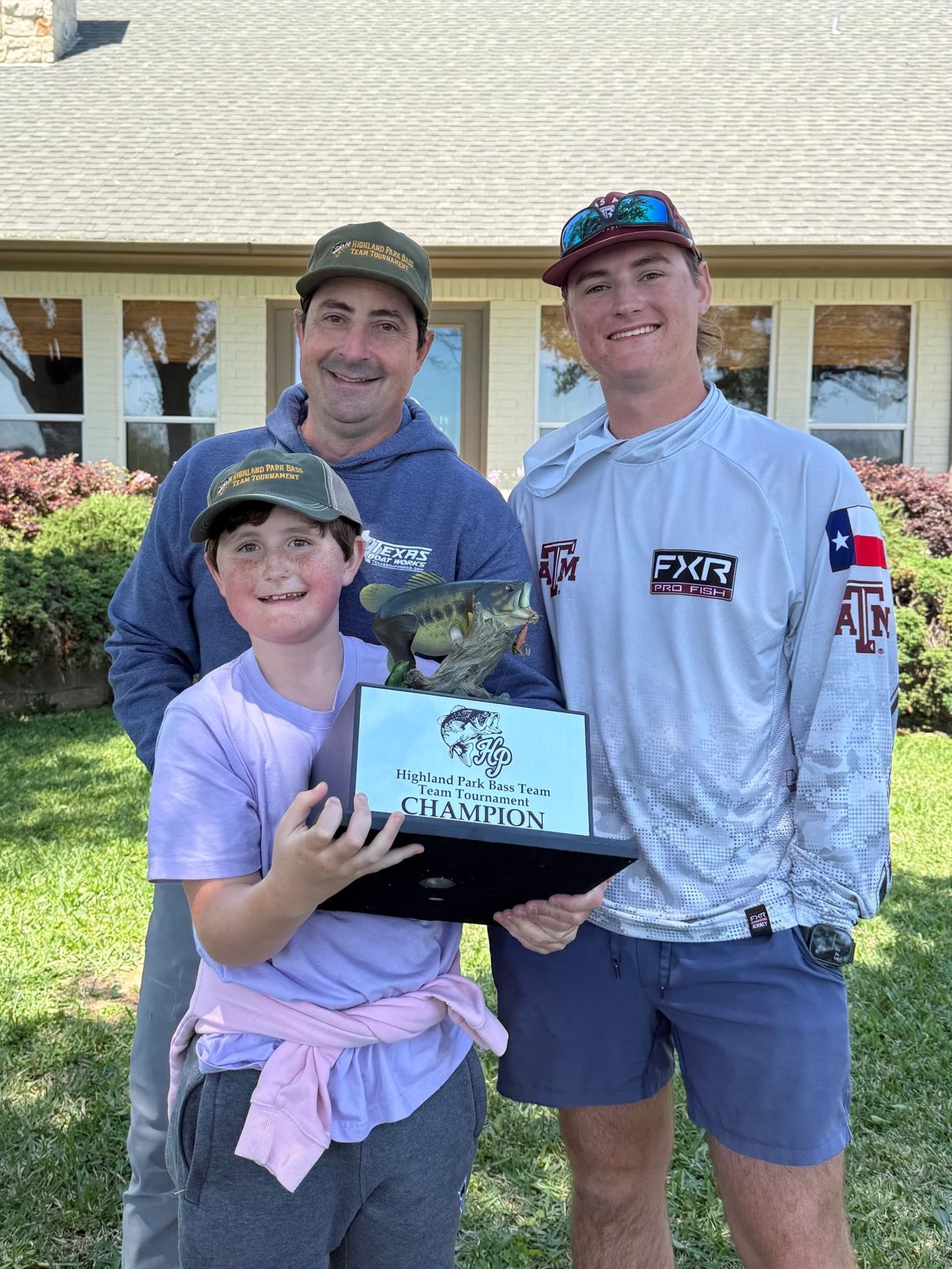 Three smiling people holding a fishing tournament trophy.