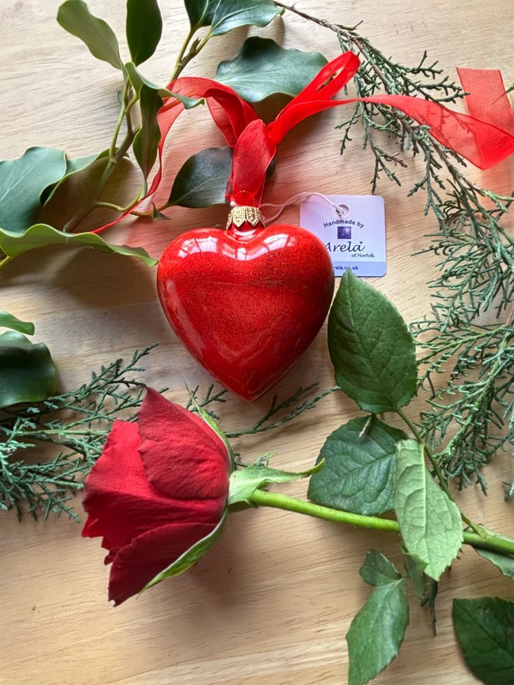 Red heart ornament and rose surrounded by green leaves on wood.