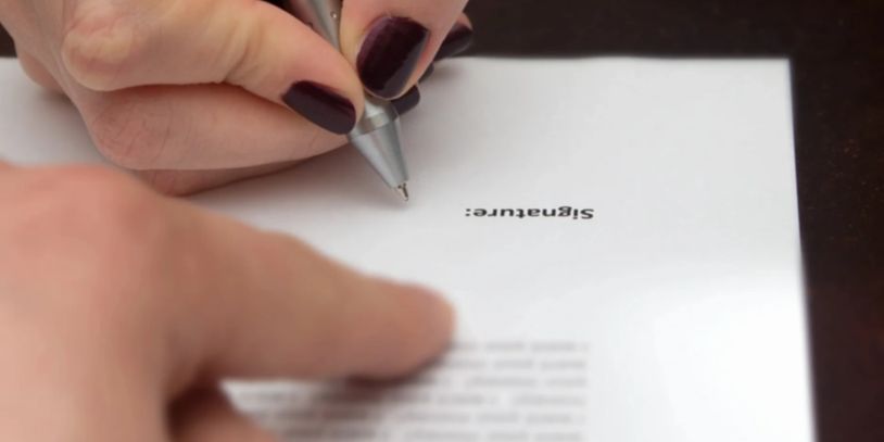 Person signing a document with a pen, focusing on the signature area.