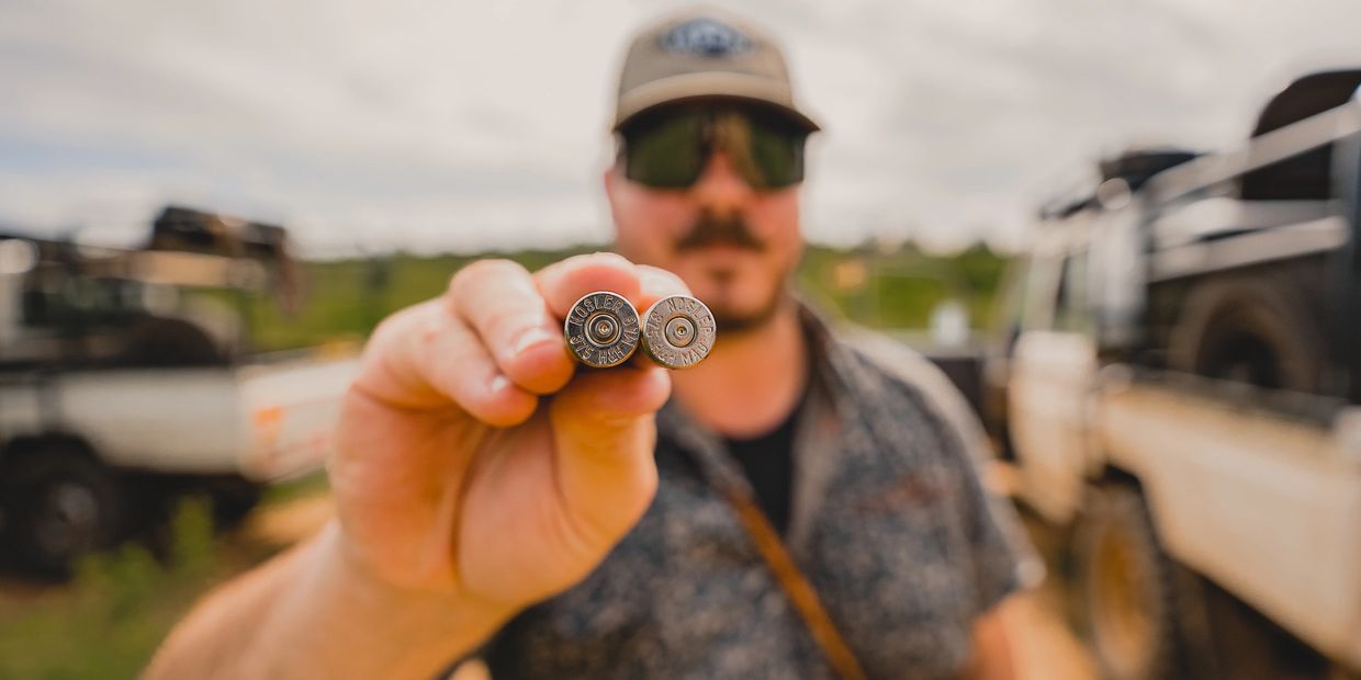 Man holding two shotgun shells close to the camera with blurred background.