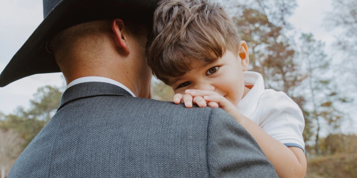 A child resting on an adult's shoulder, sharing a tender moment outdoors.