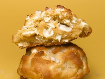 Stack of golden-brown white chocolate chip cookies with one broken in half.