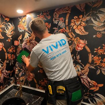Worker installing wallpaper with floral design in a bathroom.